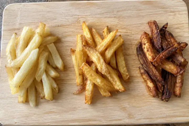 AI-generated image: Three small piles of chips on a wooden board: too pale on the left, golden in the middle, too dark on the right
