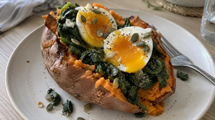 AI-generated image: Baked sweet potato split open with spinach, a halved soft-boiled egg and pumpkin seeds, a fork beside it